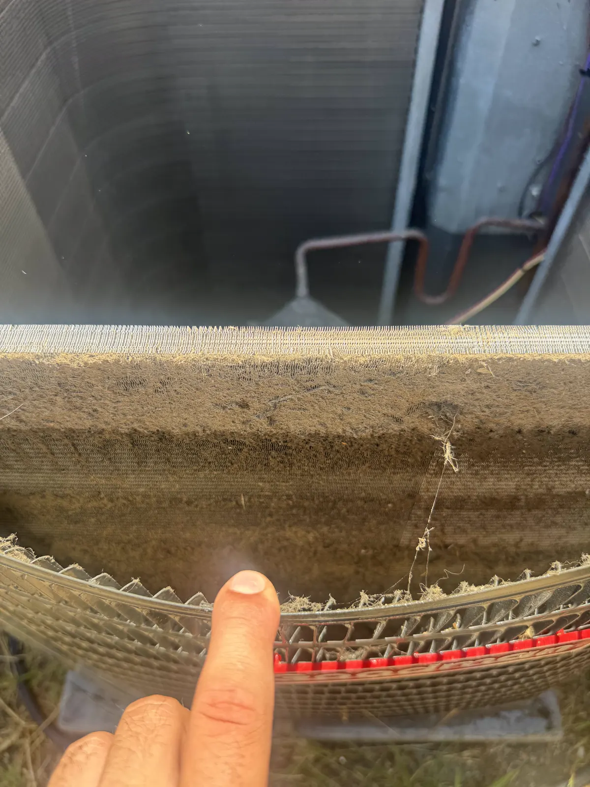 Dirty AC condenser coil in Pasadena, CA, with a finger pointing at the heavy dust buildup packed into the fins